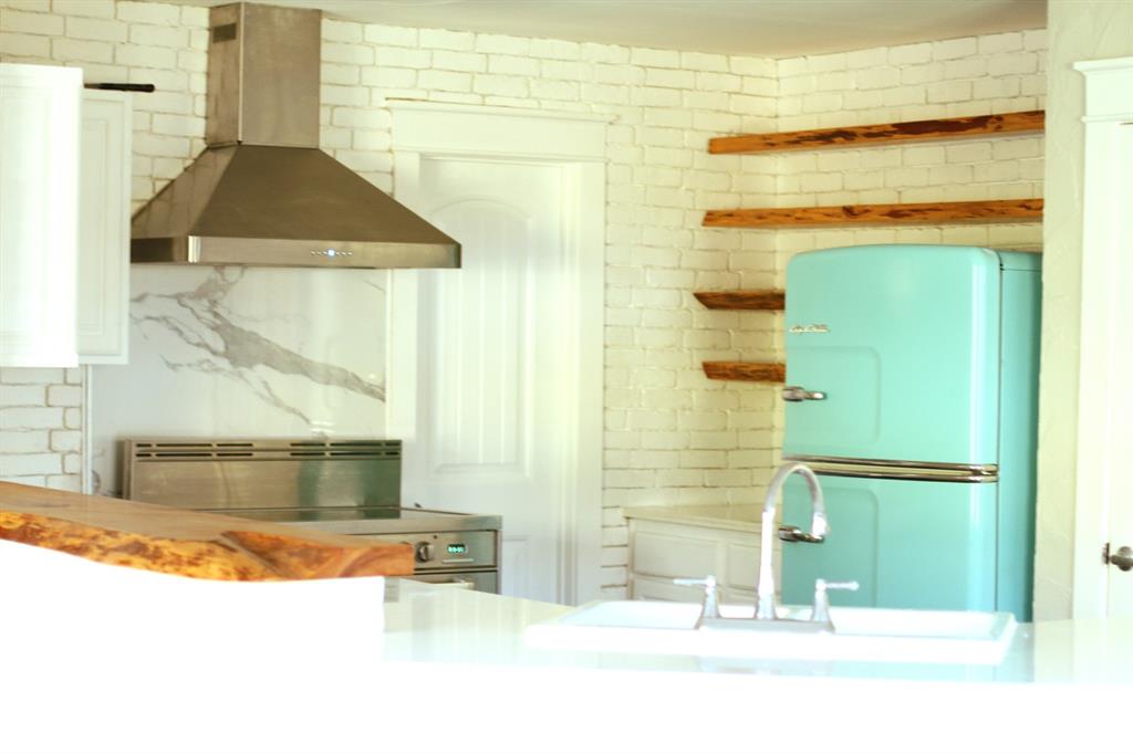 301 County Road Blossom, TX 75416 - Photo 9 of 19 Kitchen featuring a stainless steel range hood, white brick-patterned walls, a white stone-look backsplash, white cabinetry, and open wood shelving
