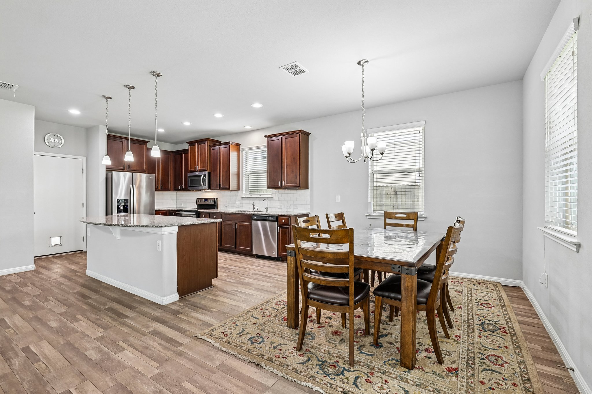 387 Guemal Road Buda, TX 78610 - Photo 1 of 39 Open-concept kitchen and dining area featuring dark wood-finish cabinetry, stainless steel appliances, a kitchen island with pendant lighting, and wood-finish flooring