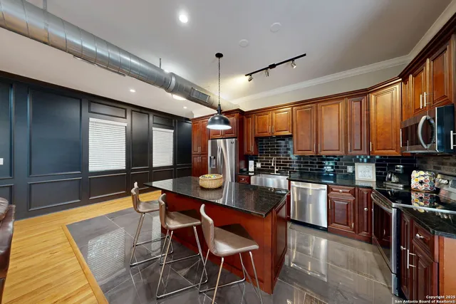a room with stainless steel appliances kitchen island granite countertop a sink and cabinets