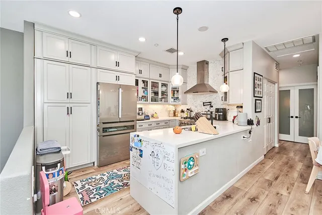 a kitchen with stainless steel appliances kitchen island granite countertop a refrigerator a sink dishwasher and white cabinets with wooden floor