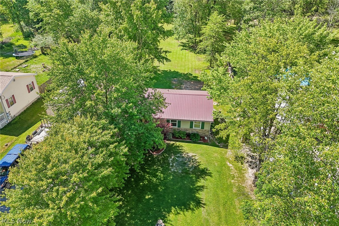 2960 Rome Rock Creek Road Rock Creek, OH 44084 - Photo 47 of 49 Residential property featuring a red metal roof, stone facade, and green shutters, surrounded by mature trees and a grassy lawn
