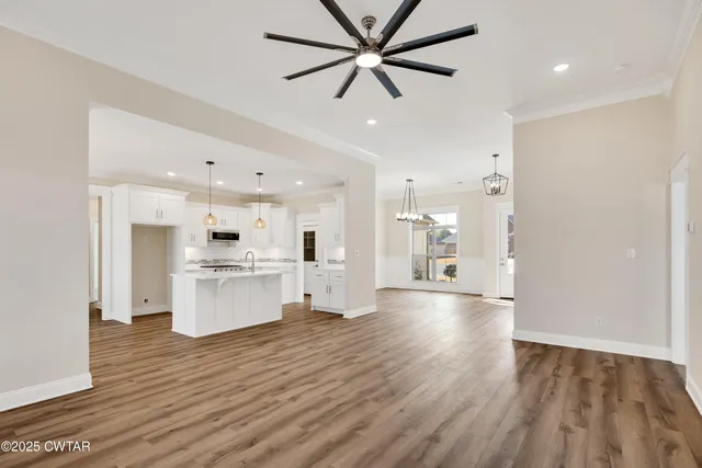 a view of an empty room and kitchen with wooden floor