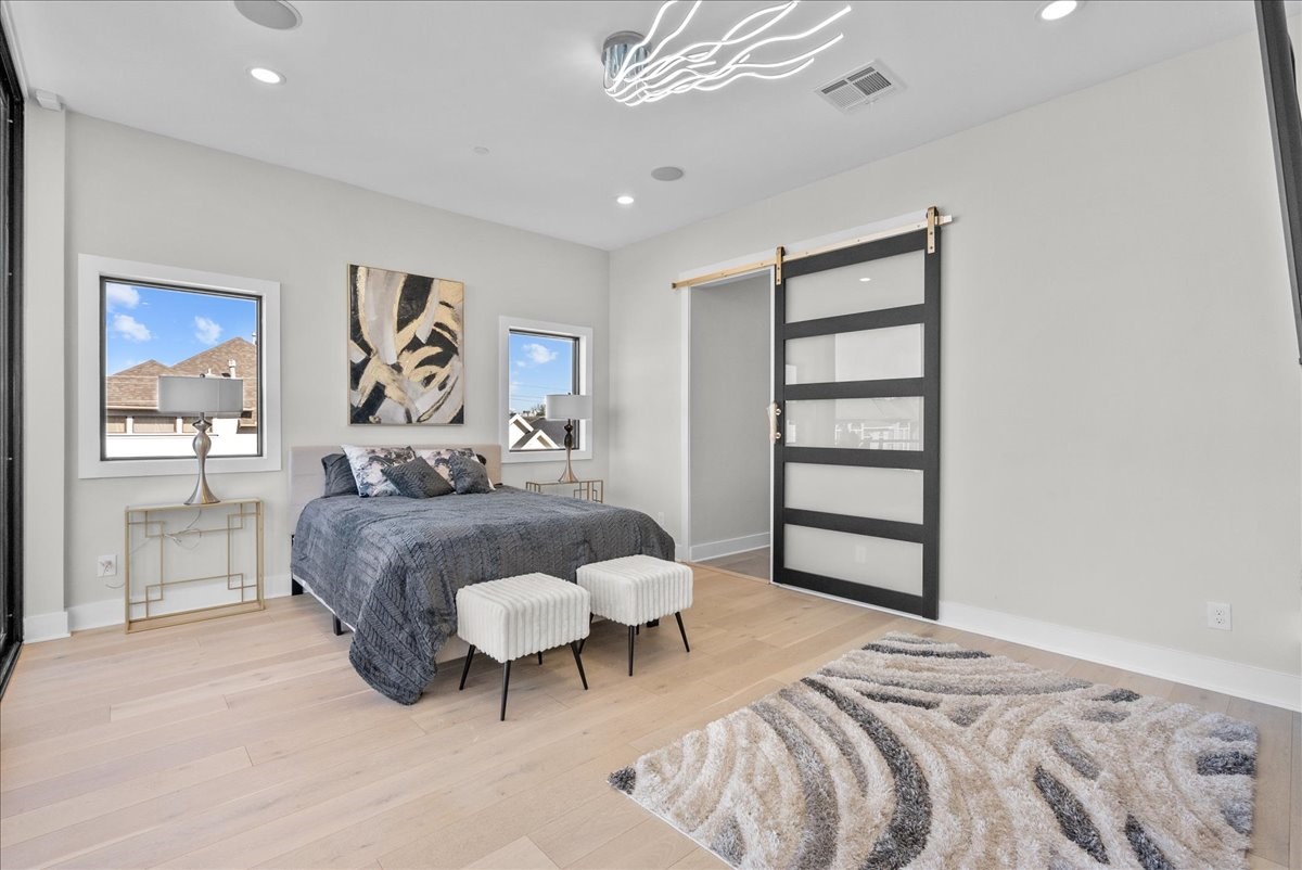 516 Reinerman Street Houston, TX 77007 - Photo 25 of 42 This bedroom features a modern design with light wood flooring, a stylish bed with dark bedding, and two windows providing natural light. A chic sliding door adds a contemporary touch, complemented by abstract artwork and elegant lighting.