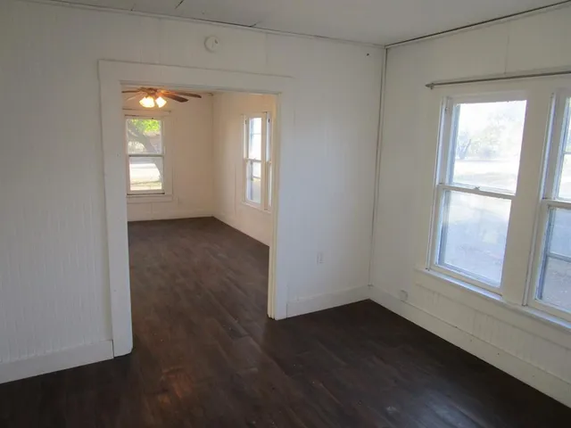 an empty room with wooden floor chandelier fan and windows