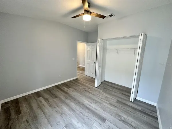 a view of an empty room with wooden floor and a ceiling fan