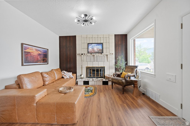 673 East 700 South Springville, UT 84663 - Photo 9 of 43 Living area featuring a white brick fireplace with a dark wood accent, wood-finish flooring, and a large window