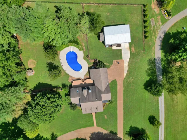 an aerial view of a residential houses with outdoor space and trees all around