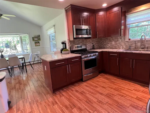 a kitchen with stainless steel appliances granite countertop wooden cabinets a stove top oven a sink and dishwasher with wooden floor