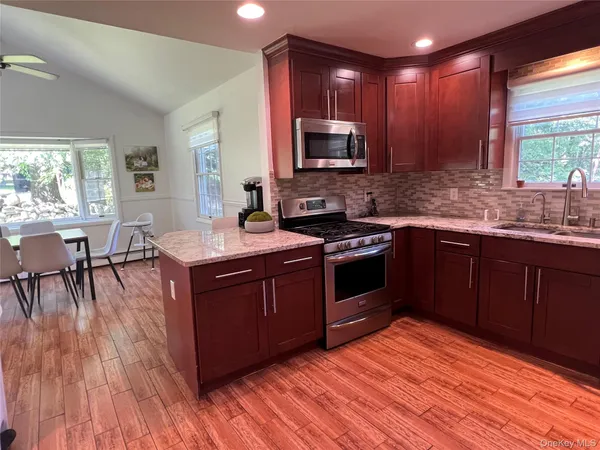 a kitchen with stainless steel appliances granite countertop wooden cabinets a stove top oven a sink and dishwasher with wooden floor