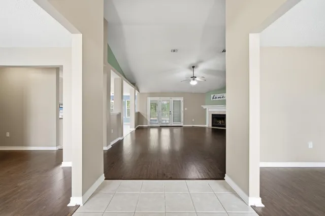 an empty room with wooden floor chandelier fan and windows