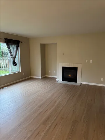 an empty room with wooden floor fire place and windows
