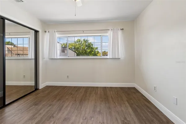 a view of an empty room with wooden floor and a ceiling fan