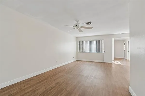 an empty room with wooden floor fan and windows