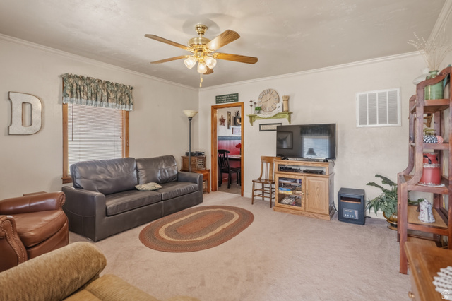 82 South 100 West Lyman, UT 84749 - Photo 12 of 27 Living area featuring light carpet, ornamental molding, and a ceiling fan