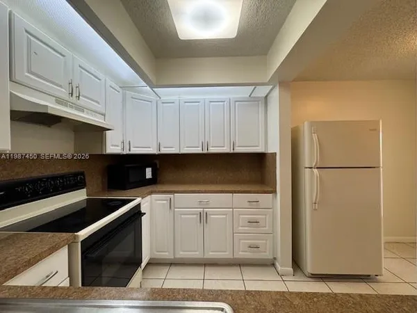 a kitchen with stainless steel appliances kitchen island granite countertop a refrigerator a stove a sink and white cabinets