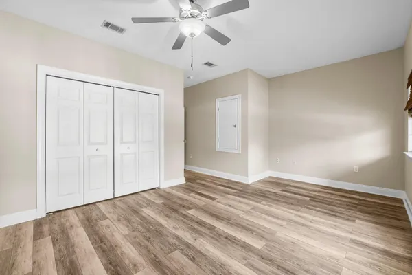a view of an empty room with wooden floor and a ceiling fan