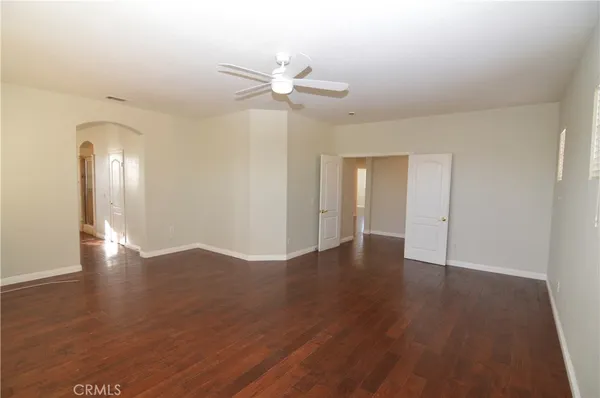 a view of an empty room with wooden floor and a ceiling fan