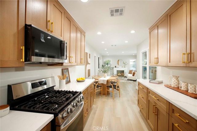 a kitchen with stainless steel appliances granite countertop a stove top oven a sink dishwasher a dining table and chairs with wooden floor