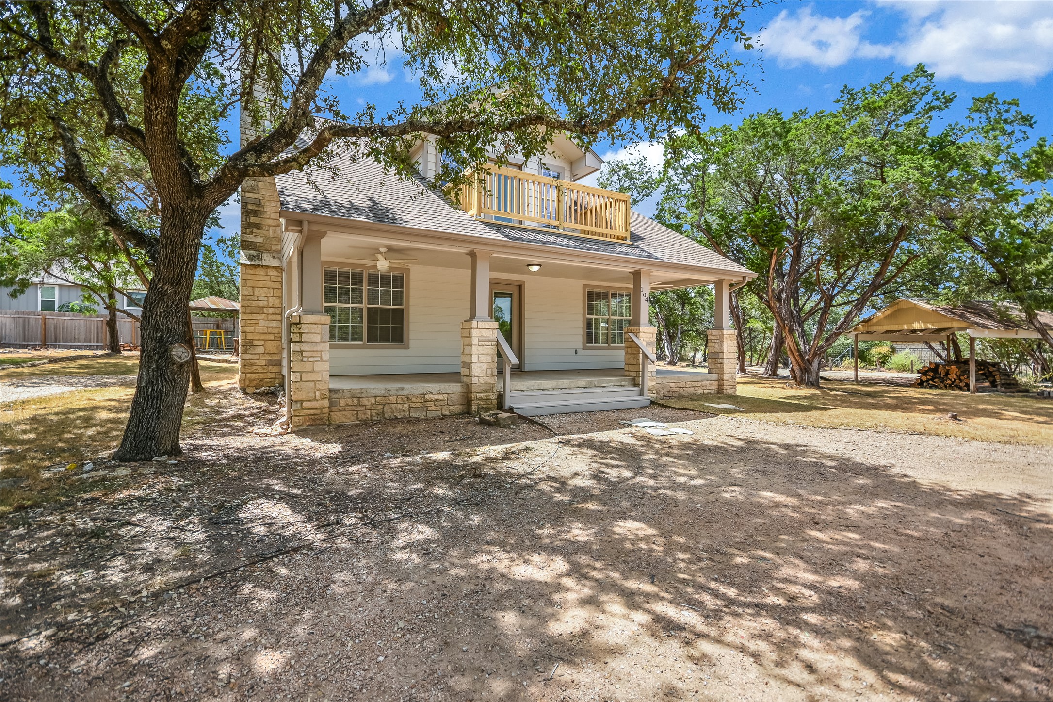 104 Crazy Cross Road Wimberley, TX 78676 - Photo 2 of 20 Mature trees shade a welcoming front porch supported by robust stone pillars.