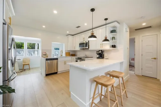 a kitchen with stainless steel appliances kitchen island granite countertop a stove a sink a refrigerator and white cabinets with wooden floor