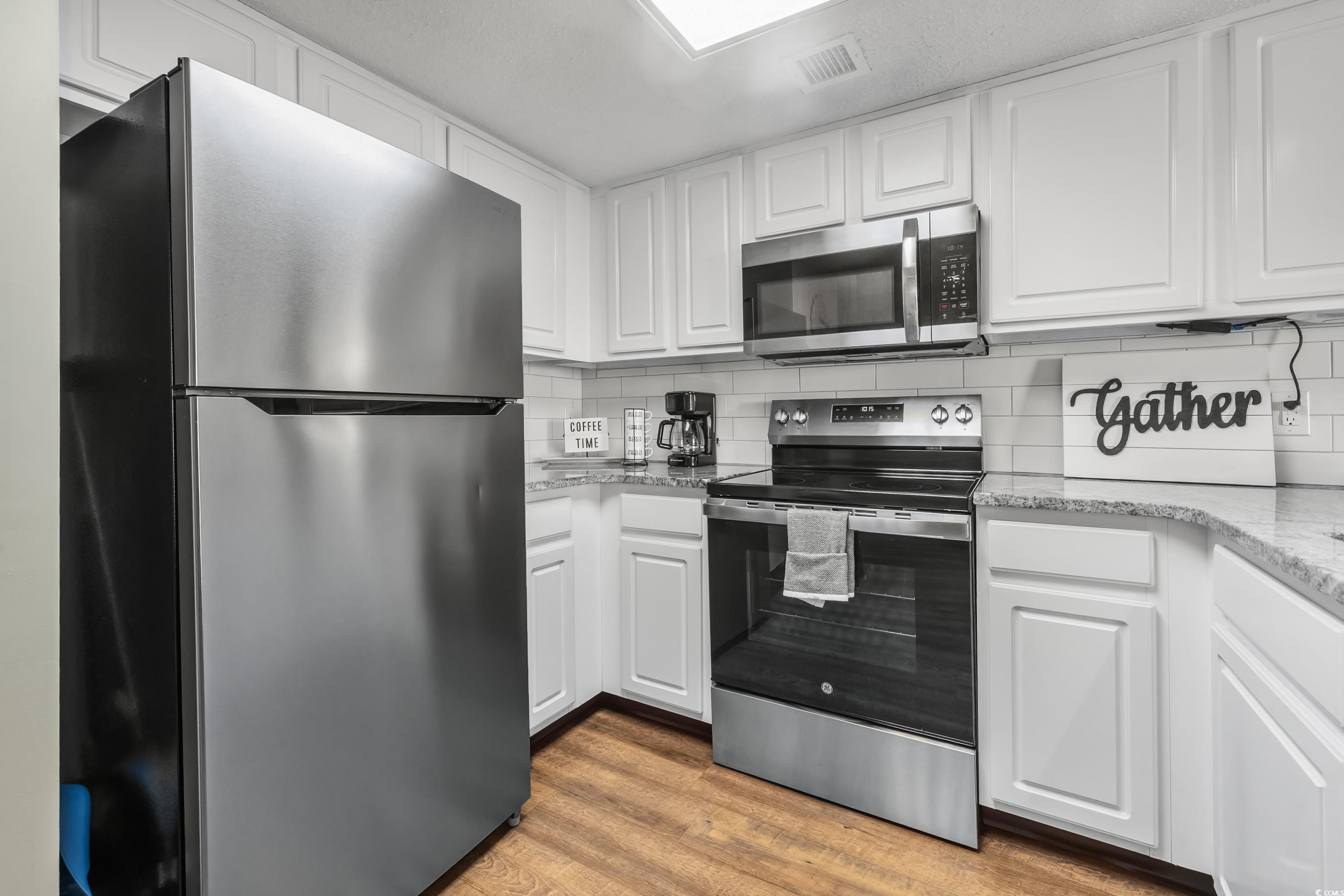 205 74th Avenue North, Unit 1104 Myrtle Beach, SC 29572 - Photo 16 of 40 Kitchen featuring appliances with stainless steel finishes, white cabinetry, dark wood-type flooring, light stone countertops, and decorative backsplash