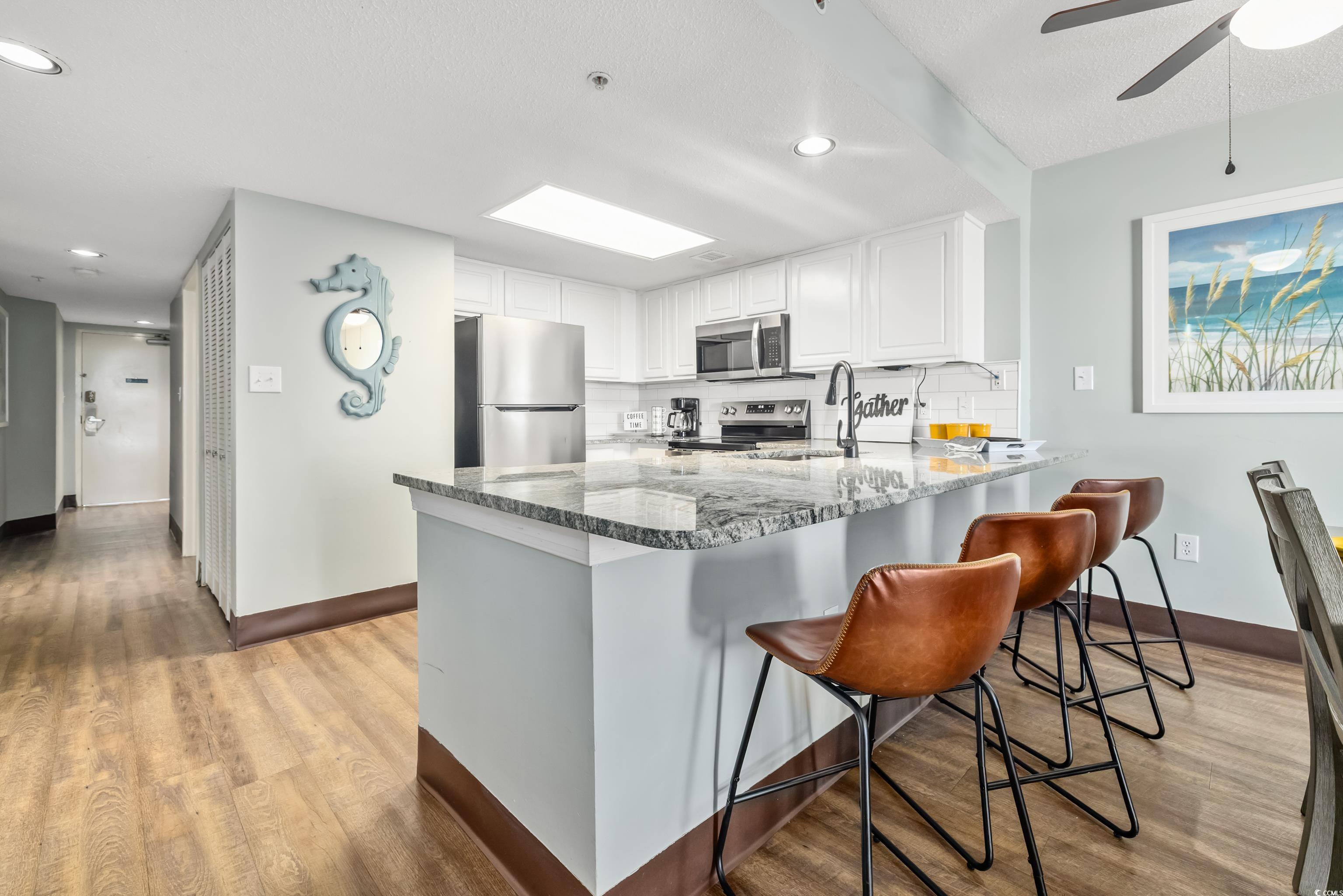 205 74th Avenue North, Unit 1104 Myrtle Beach, SC 29572 - Photo 17 of 40 Kitchen featuring white cabinets, a peninsula, light wood-style flooring, stainless steel appliances, and dark stone counters