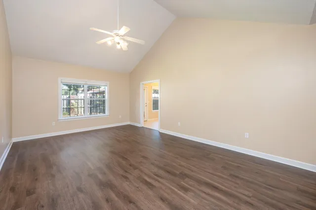 an empty room with wooden floor chandelier fan and windows