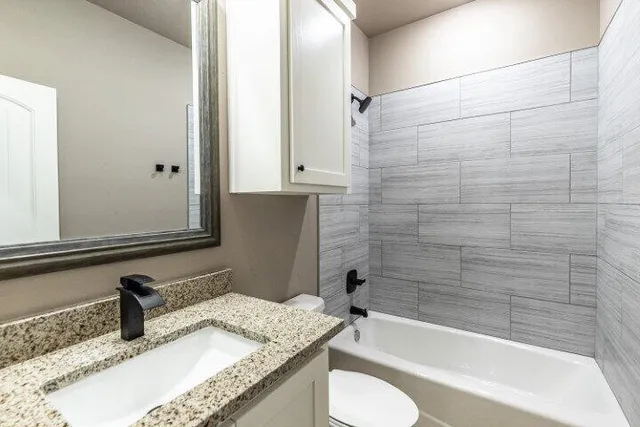 a bathroom with a granite countertop bathtub sink vanity mirror and toilet