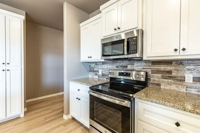 a kitchen with stainless steel appliances granite countertop white cabinets granite counter tops and a wooden floors