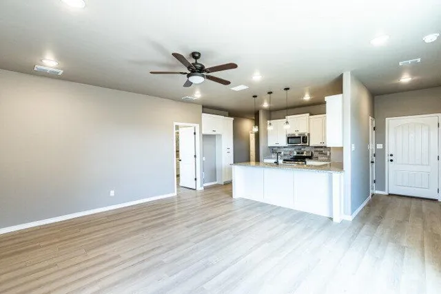 a view of an empty room and kitchen with wooden floor