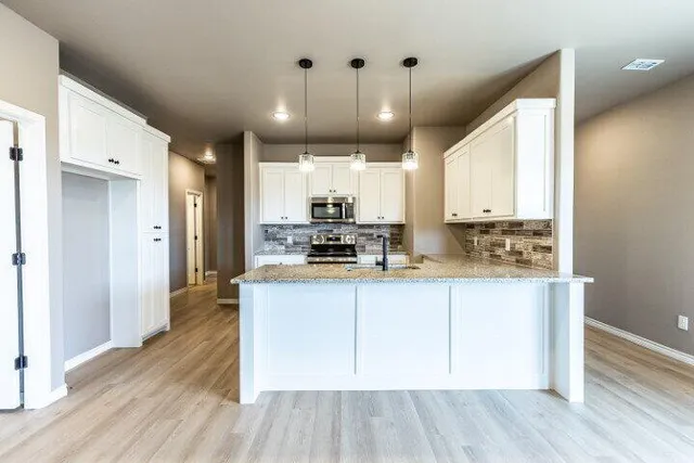 a kitchen with stainless steel appliances granite countertop a refrigerator a sink dishwasher a stove and white cabinets with wooden floor