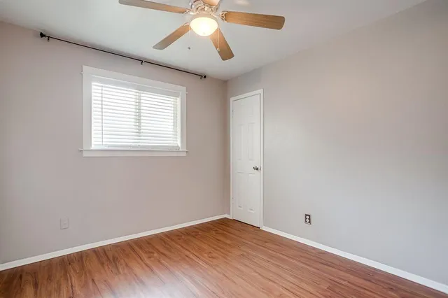 an empty room with wooden floor chandelier fan and windows