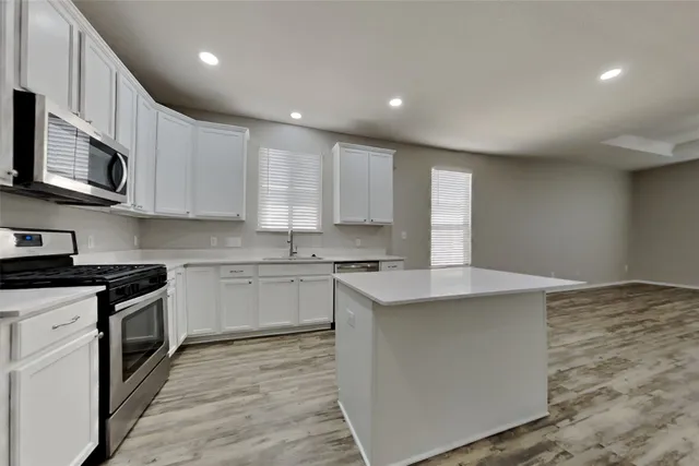 a kitchen with stainless steel appliances granite countertop a stove top oven a sink dishwasher and a microwave oven with wooden floor