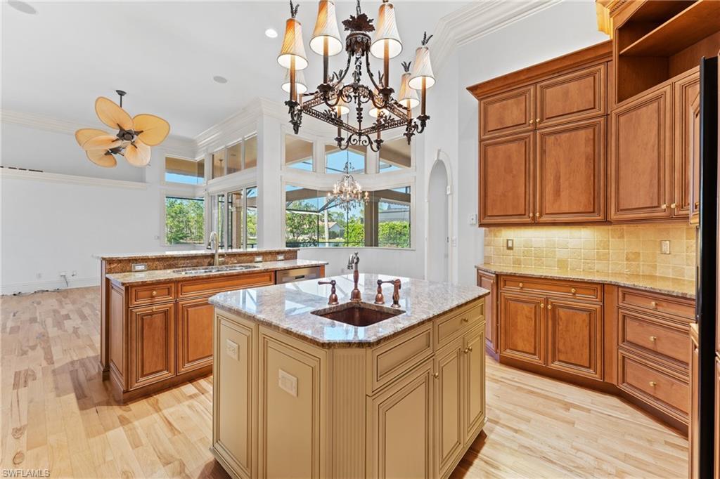 7126 Mill Run Road Naples, FL 34109 - Photo 12 of 49 Kitchen featuring light stone counters, ornamental molding, ceiling fan with notable chandelier, a kitchen island with sink, and pendant lighting