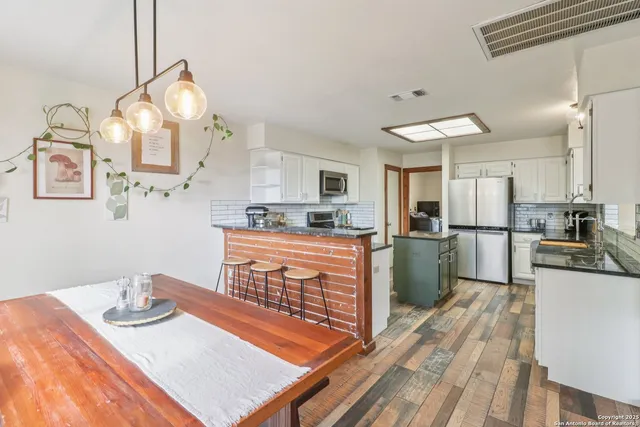 a kitchen with stainless steel appliances granite countertop a refrigerator a sink dishwasher a stove and white cabinets with wooden floor