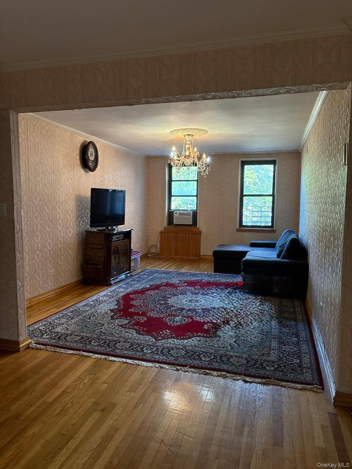84-01 Main Street, Unit 311 Queens, NY 11435 - Photo 1 of 1 Living room featuring wood-type flooring, wallpapered walls, ornamental molding, and a chandelier