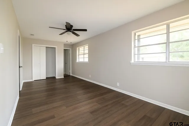 an empty room with wooden floor ceiling fan and windows