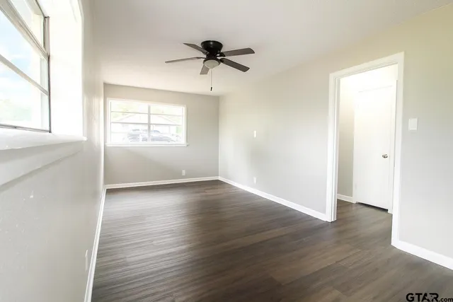 an empty room with wooden floor chandelier fan and windows