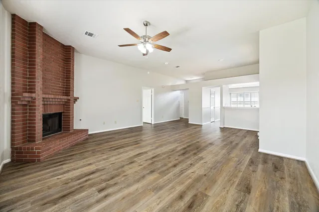 an empty room with wooden floor fireplace and windows