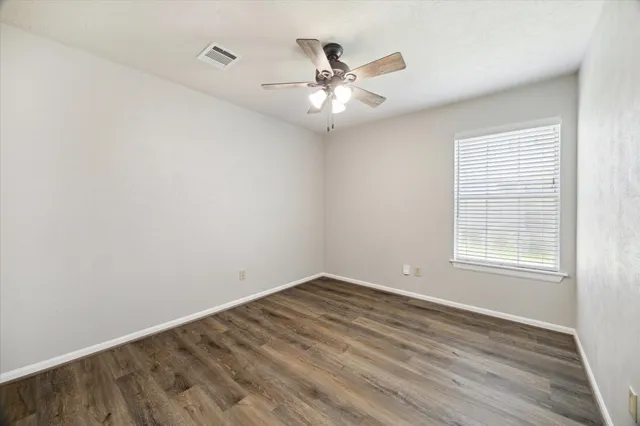 an empty room with wooden floor fan and windows