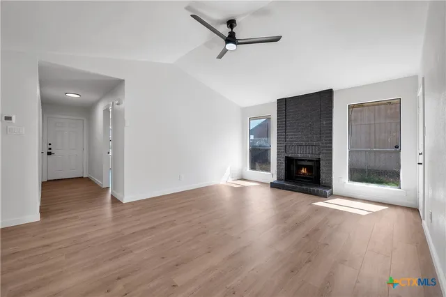 an empty room with wooden floor a fireplace and windows