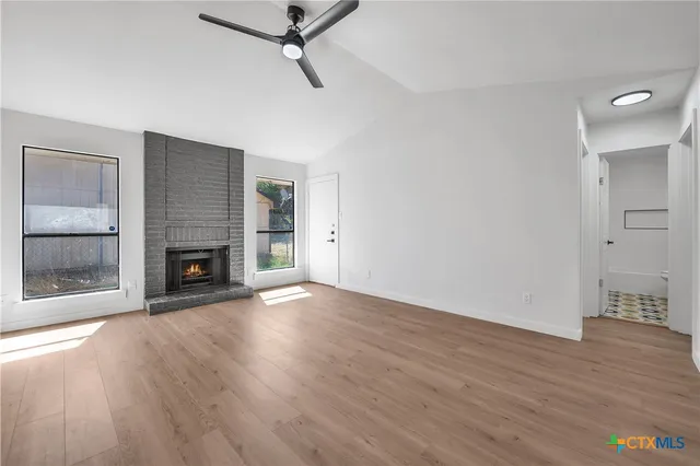 an empty room with wooden floor fireplace and windows