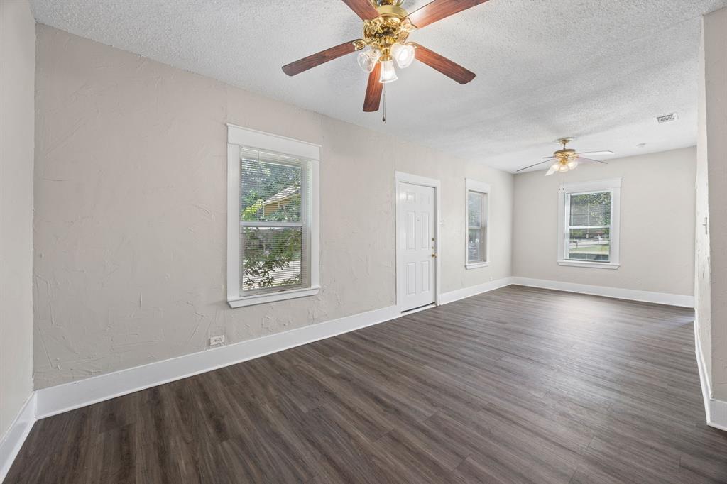 705 Madison Street Cleburne, TX 76033 - Photo 7 of 26 an empty room with wooden floor chandelier fan and windows