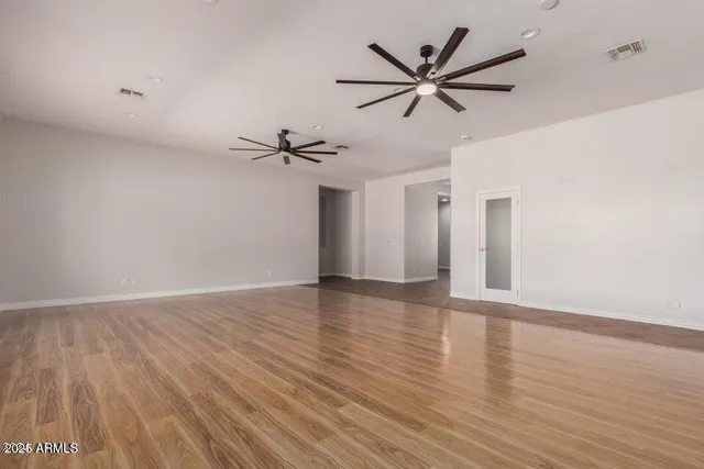 a view of an empty room with wooden floor and a ceiling fan