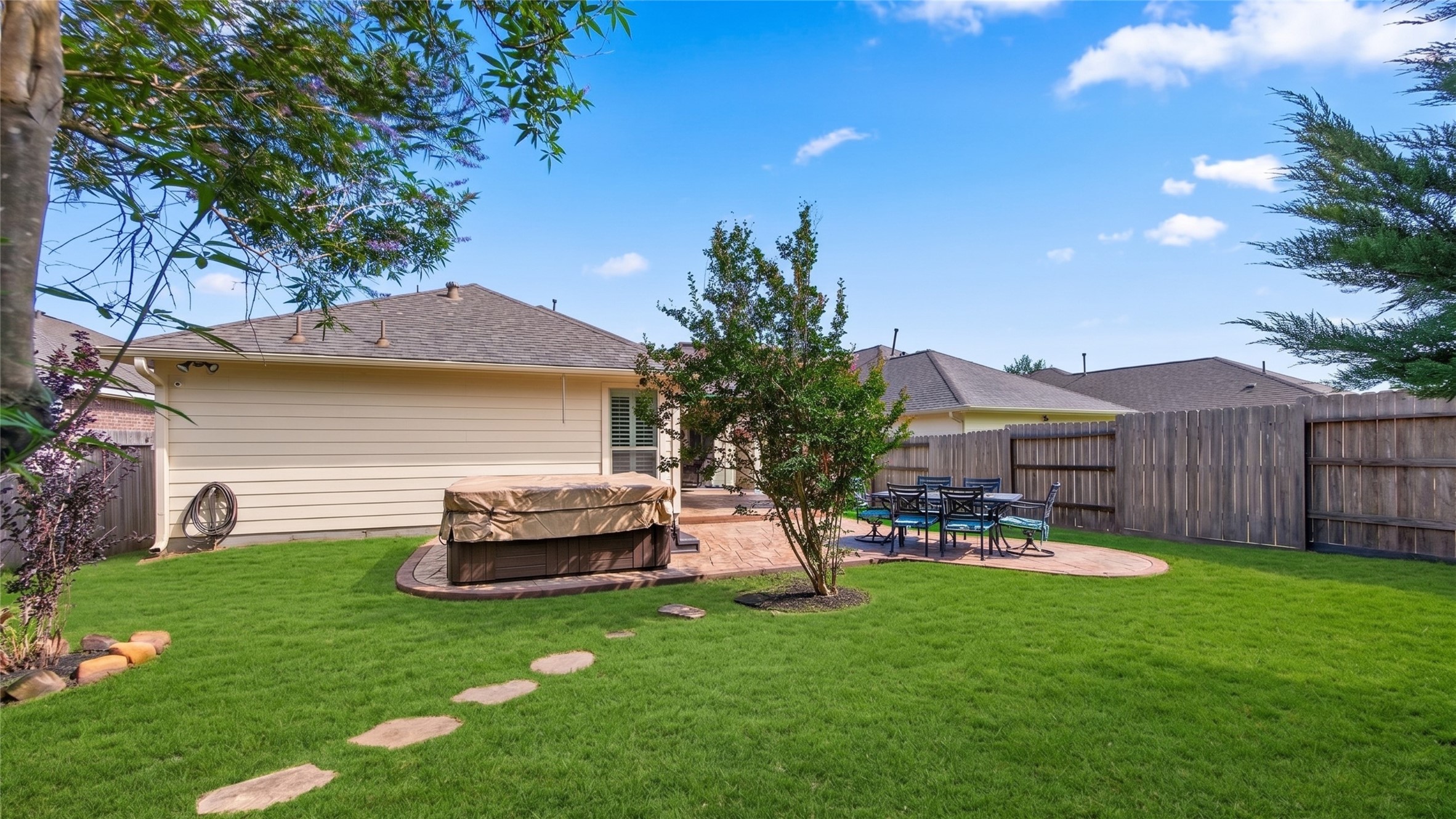 27443 Rebecca Field Lane Spring, TX 77386 - Photo 26 of 31 This backyard features a well-maintained lawn with a stepping stone path leading to a patio area. It's equipped with a hot tub and outdoor dining set, perfect for relaxation and entertaining. The space is enclosed by a wooden fence, providing privacy.