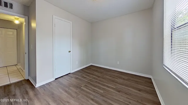 a view of an empty room with wooden floor and a window