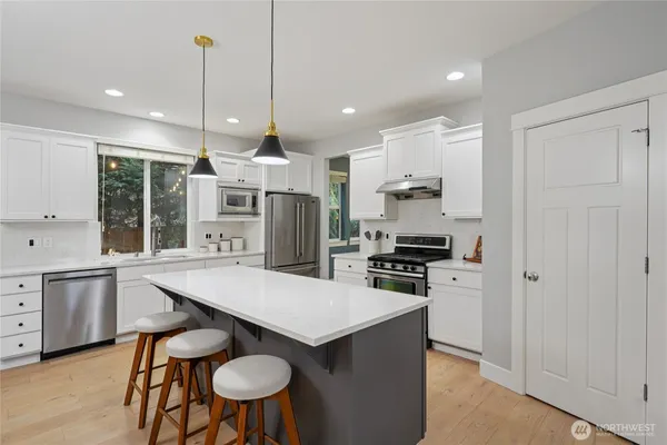 a kitchen with stainless steel appliances granite countertop a stove top oven a refrigerator a sink and chairs