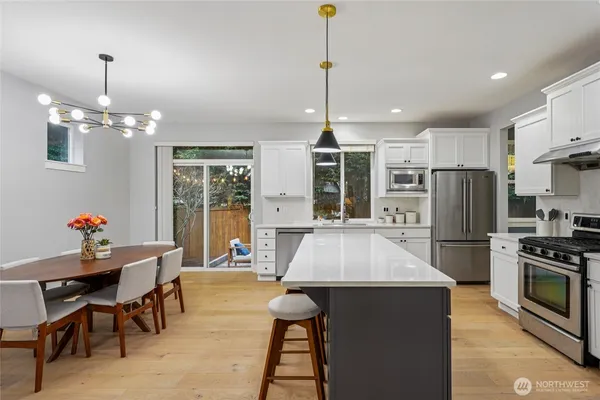 a kitchen with stainless steel appliances kitchen island granite countertop a refrigerator a stove top oven a dining table and chairs with wooden floor
