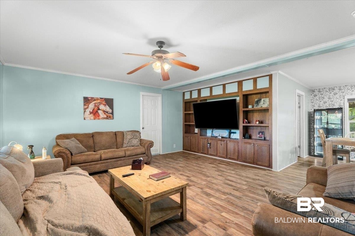 21011 River Road Robertsdale, AL 36567 - Photo 4 of 29 Living area featuring wood-finish flooring, a built-in media center with shelving, a ceiling fan, light blue wall paint, and white trim