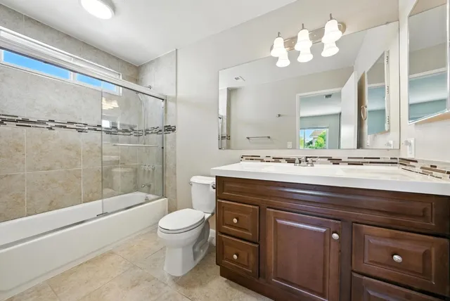 a bathroom with a granite countertop sink a toilet a mirror and shower